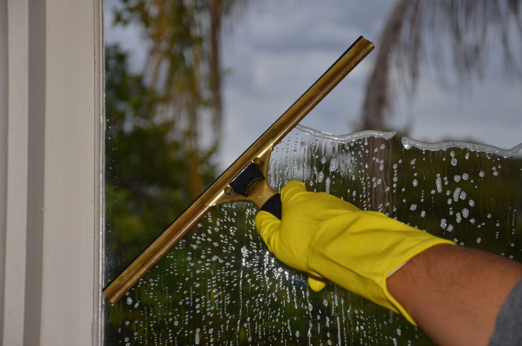 person cleaning window with squeegee and gloves